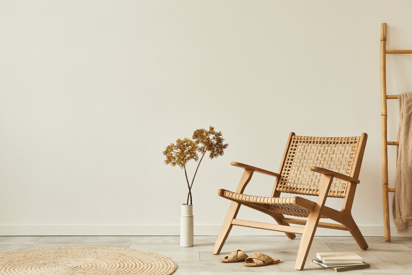 Neutral concept of living room interior with design wooden armchair, round carpet, dried flowers in vase, slippers, decoration and elegant personal accessories. Template. Copy space.